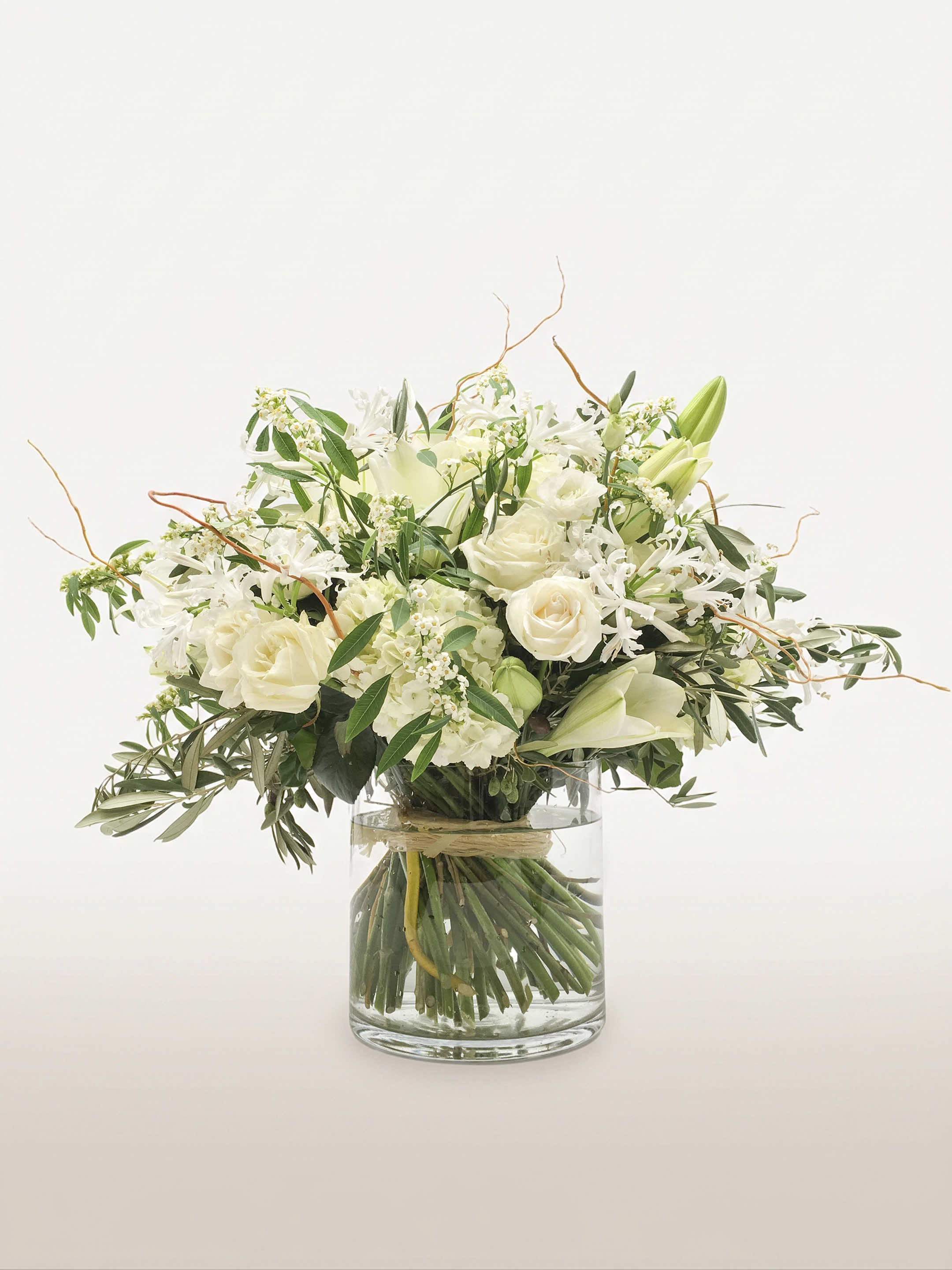 Jardin de Monet dans un vase cylindrique, roses blanches, lys et branches courbées émergeant du feuillage