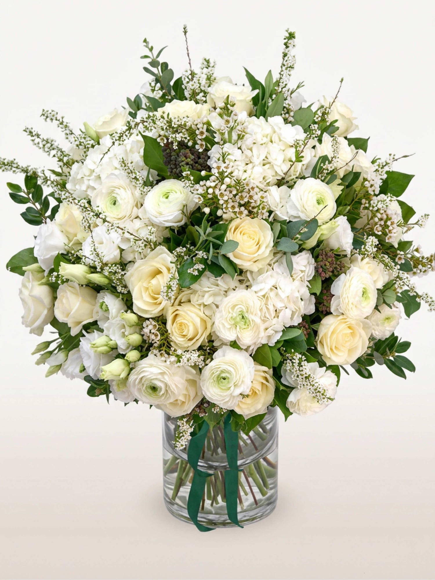 Reine Blanche L, roses, renoncules et hortensias blancs mêlés de feuillage dans un vase en verre