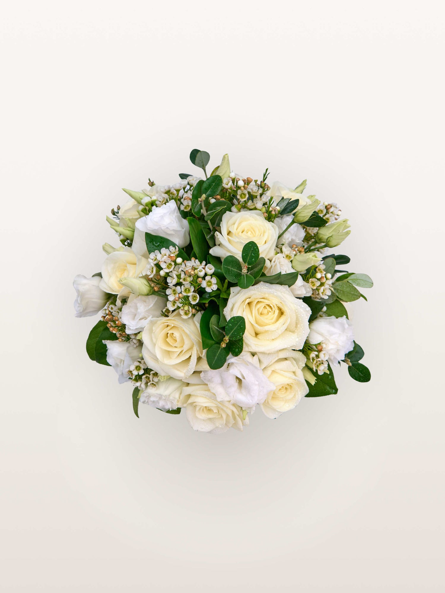 Reine Blanche S, roses ivoire, lisianthus blancs et fleurs de cire parmi un feuillage vert