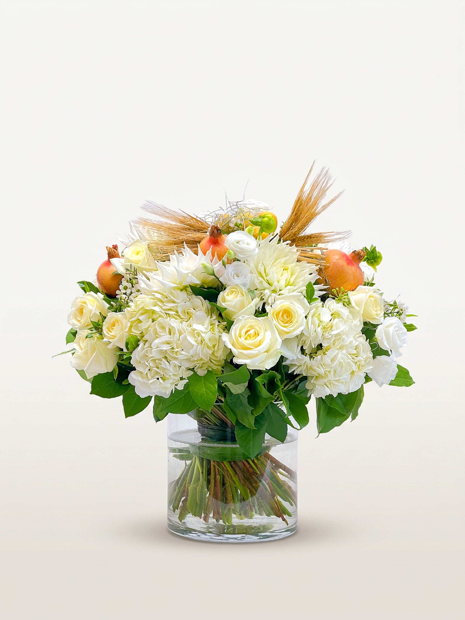 Roses blanches et crème, hortensias, dahlias, grenades, épis de blé et feuillage vert dans un vase cylindrique