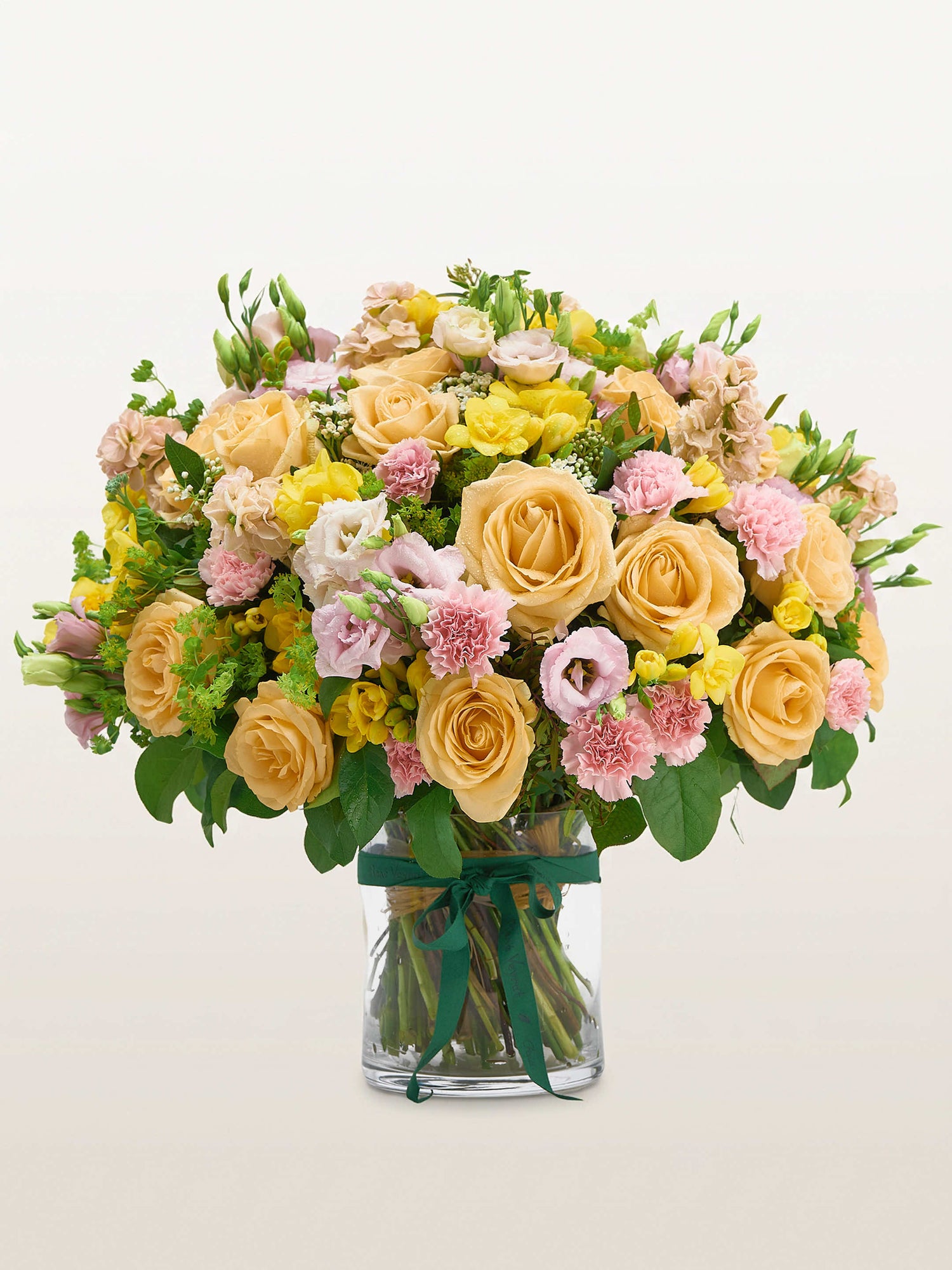 Point du Jour L, roses abricot, œillets roses et lisianthus dans un vase en verre noué de ruban vert