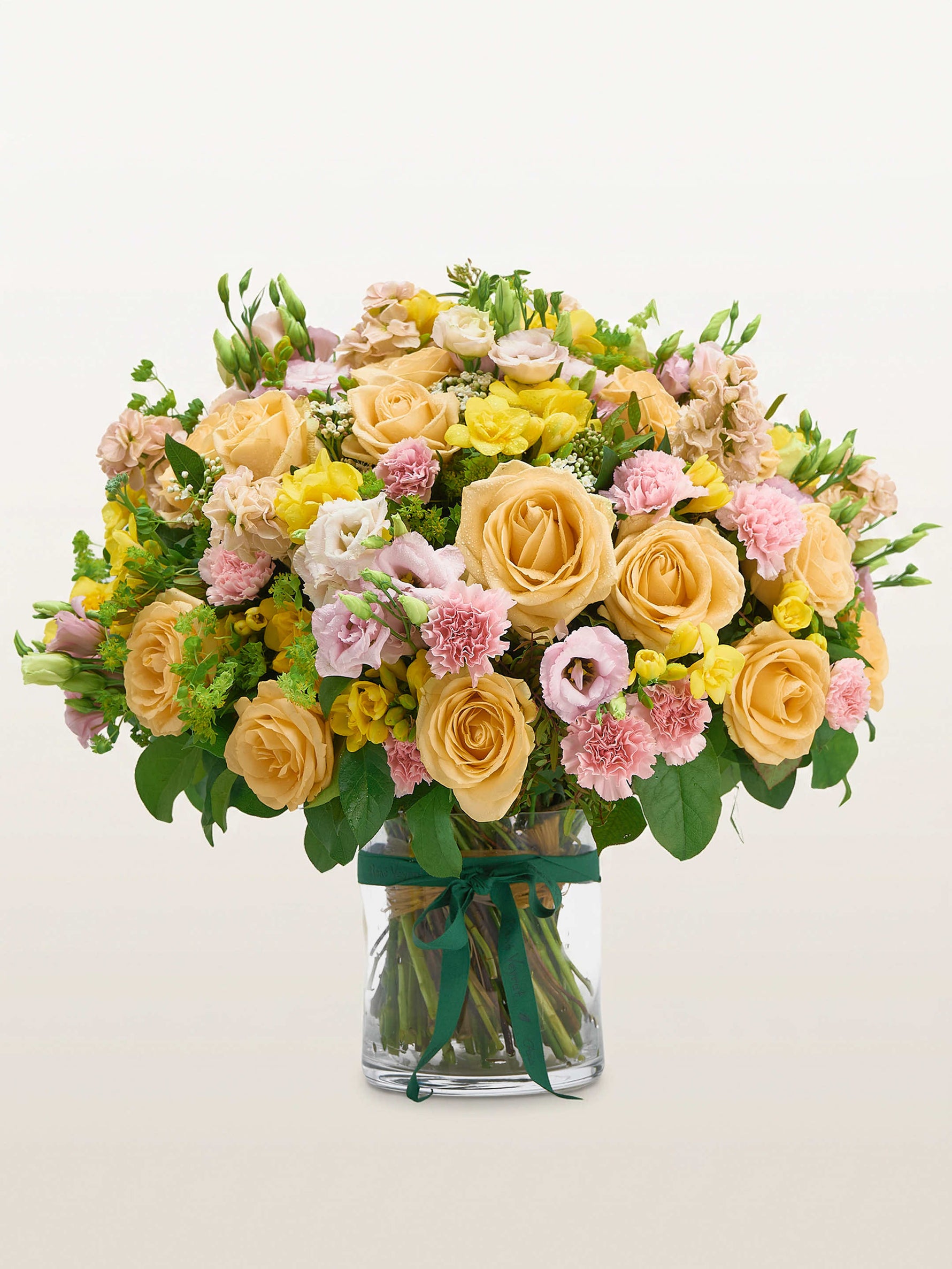 Point du Jour L, roses abricot, œillets roses et lisianthus dans un vase en verre noué de ruban vert