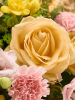 Point du Jour M, rose pêche perlée de gouttes entourée d'œillets roses et de roses jaunes