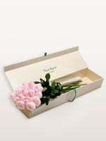Coffret Princesse ivoire ouvert, quinze roses roses aux tiges vertes reposant sur papier de soie blanc