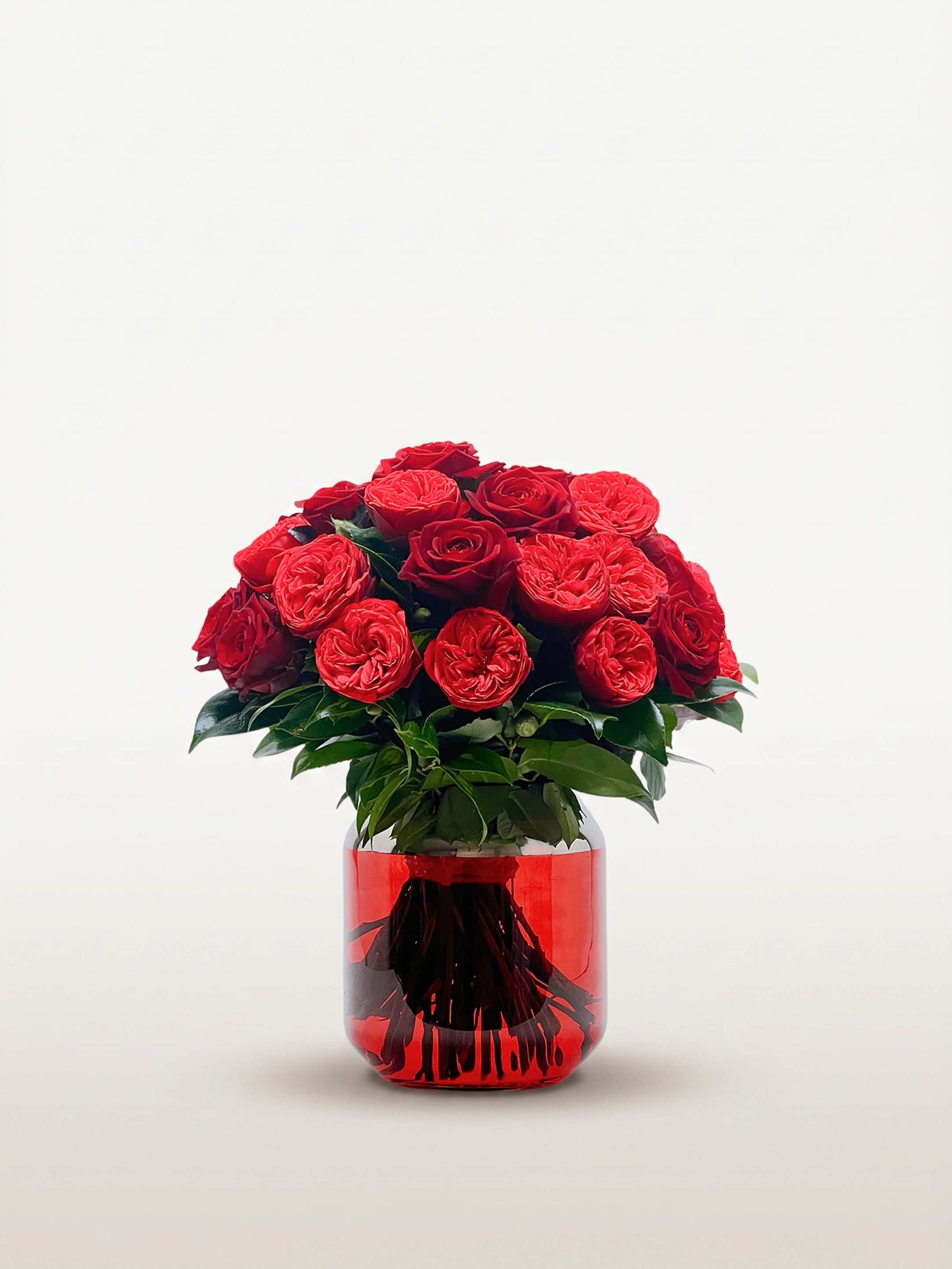 Bouquet rond Cornaline de trente roses rouges et cramoisies, feuillage vert dans un vase rouge translucide