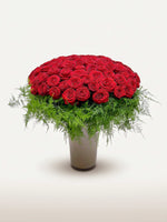 Royal N°100 déploie une brassée XXL de roses rouges en dôme, entourées de fougères retombantes dans un vase ivoire