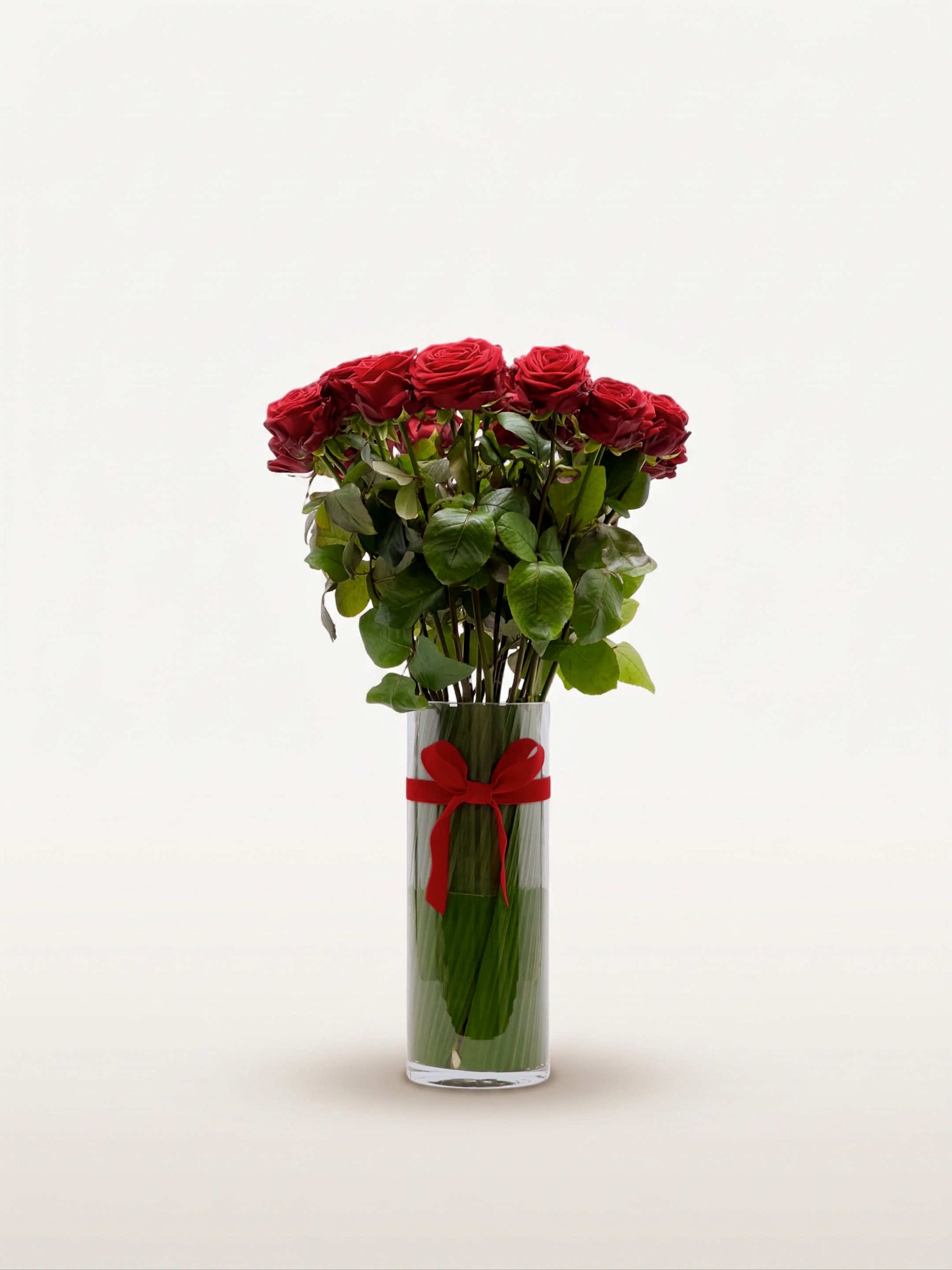 Royal N°25 rassemble une brassée de roses rouges veloutées dans un vase cylindrique en verre, noué d'un ruban rouge