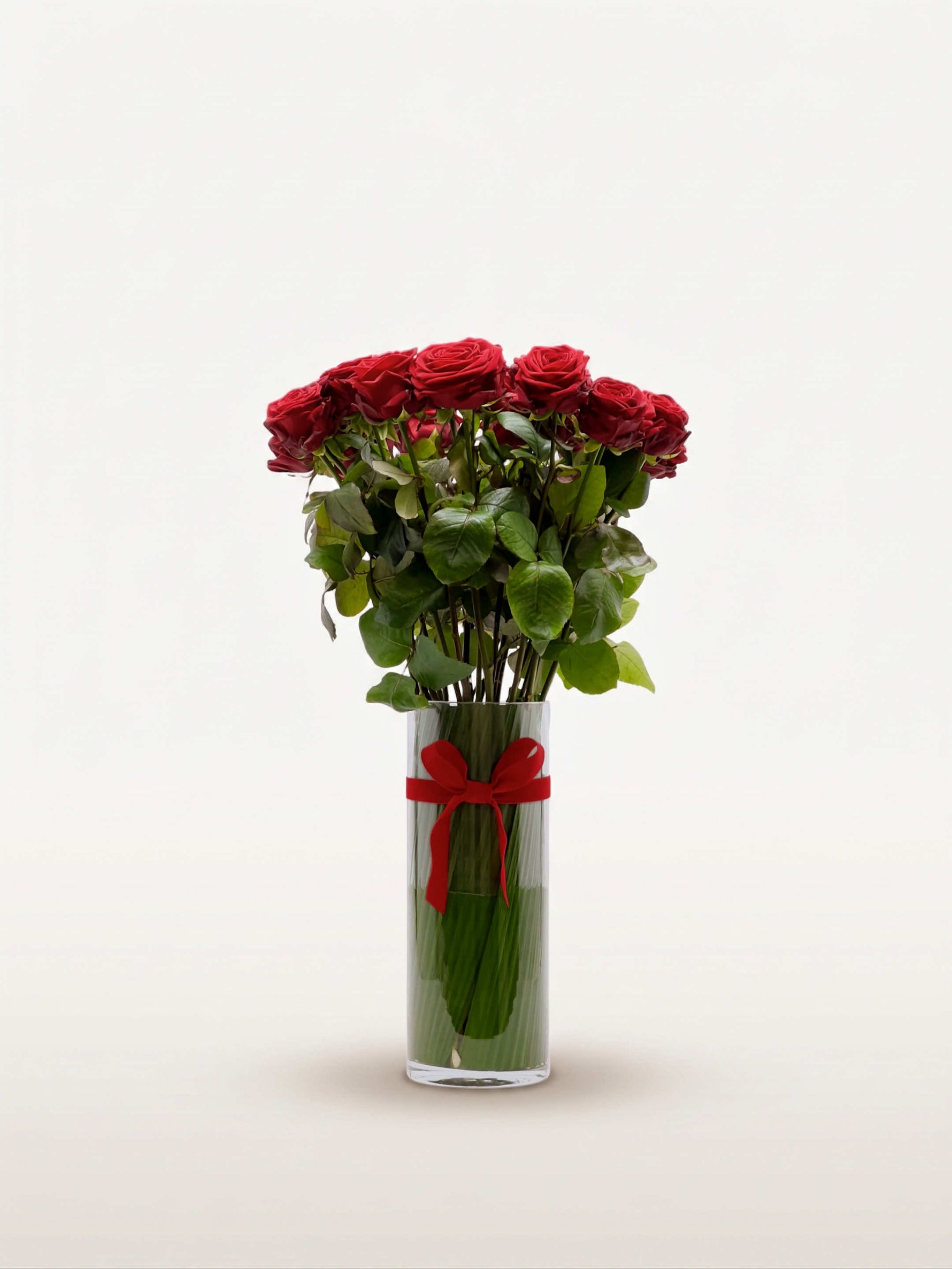 Royal N°25 rassemble une brassée de roses rouges veloutées dans un vase cylindrique en verre, noué d'un ruban rouge