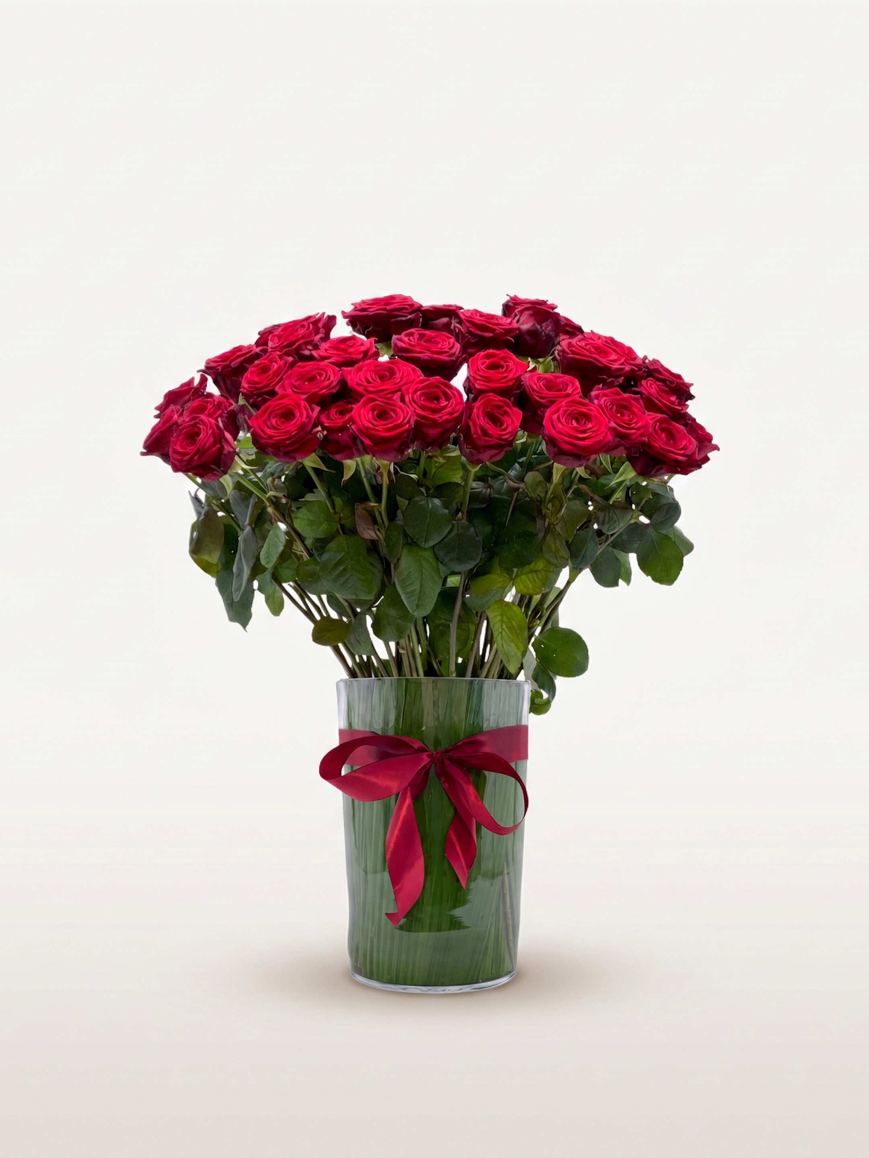 Royal N°50 rassemble une brassée de roses rouges dans un vase en verre orné d'un ruban bordeaux noué
