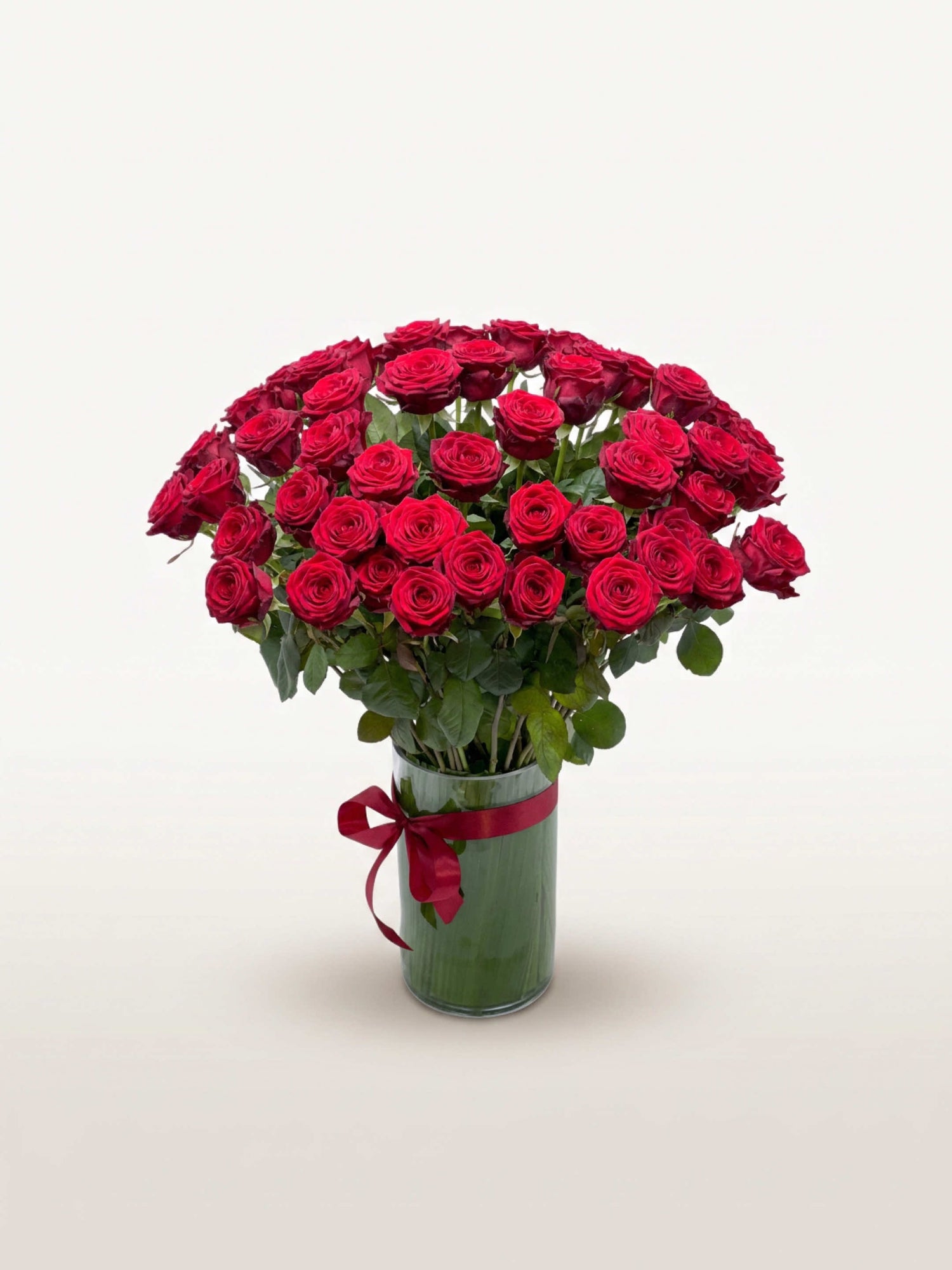 Royal N°50 réunit une brassée généreuse de roses rouges veloutées dans un vase en verre noué d'un ruban rouge