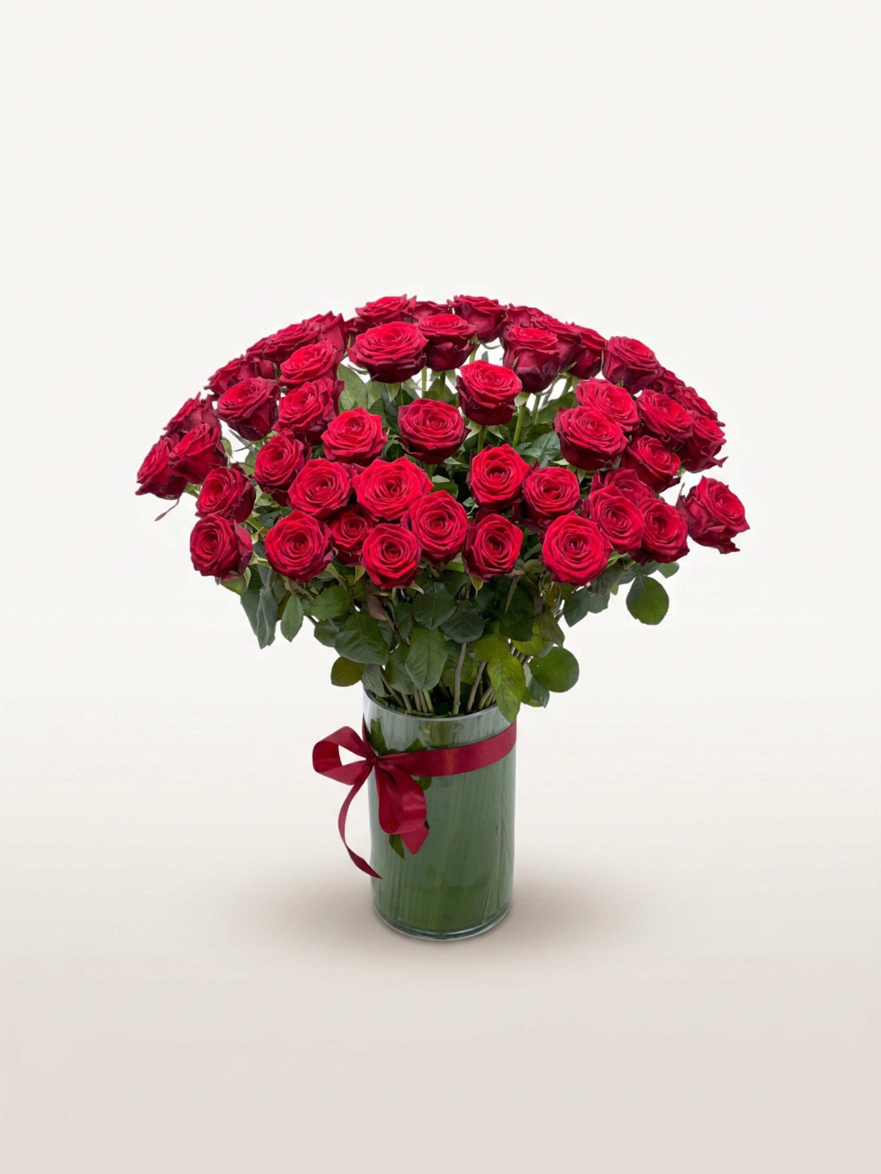 Royal N°50 réunit une brassée généreuse de roses rouges veloutées dans un vase en verre noué d'un ruban rouge